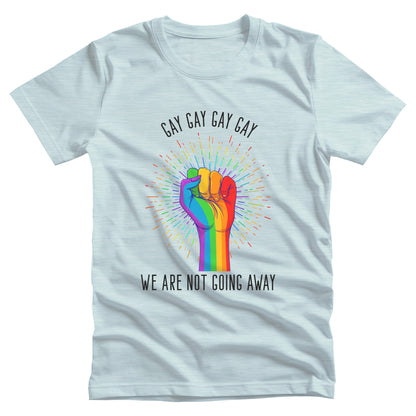 Heather Ice Blue color unisex t-shirt that says, “Gay Gay Gay Gay We Are Not Going Away” with a graphic of a rainbow fist with a thin, rainbow-colored starburst behind it. Arched over the top of the starburst are the words “Gay Gay Gay Gay” in all caps. The rest of the text is beneath the graphic on one horizontal line.