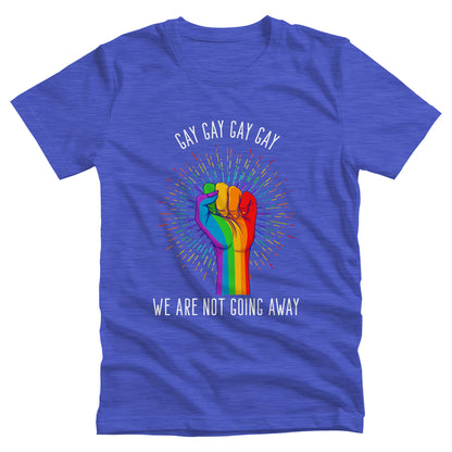 Heather True Royal  color unisex t-shirt that says, “Gay Gay Gay Gay We Are Not Going Away” with a graphic of a rainbow fist with a thin, rainbow-colored starburst behind it. Arched over the top of the starburst are the words “Gay Gay Gay Gay” in all caps. The rest of the text is beneath the graphic on one horizontal line.