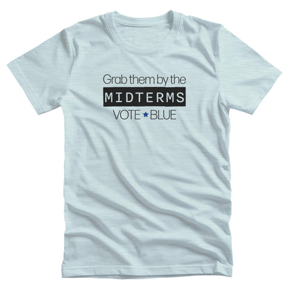 Heather Ice Blue color unisex t-shirt that say, “Grab them by the midterms. Vote Blue.” The word “Midterms” is in a black rectangle. 