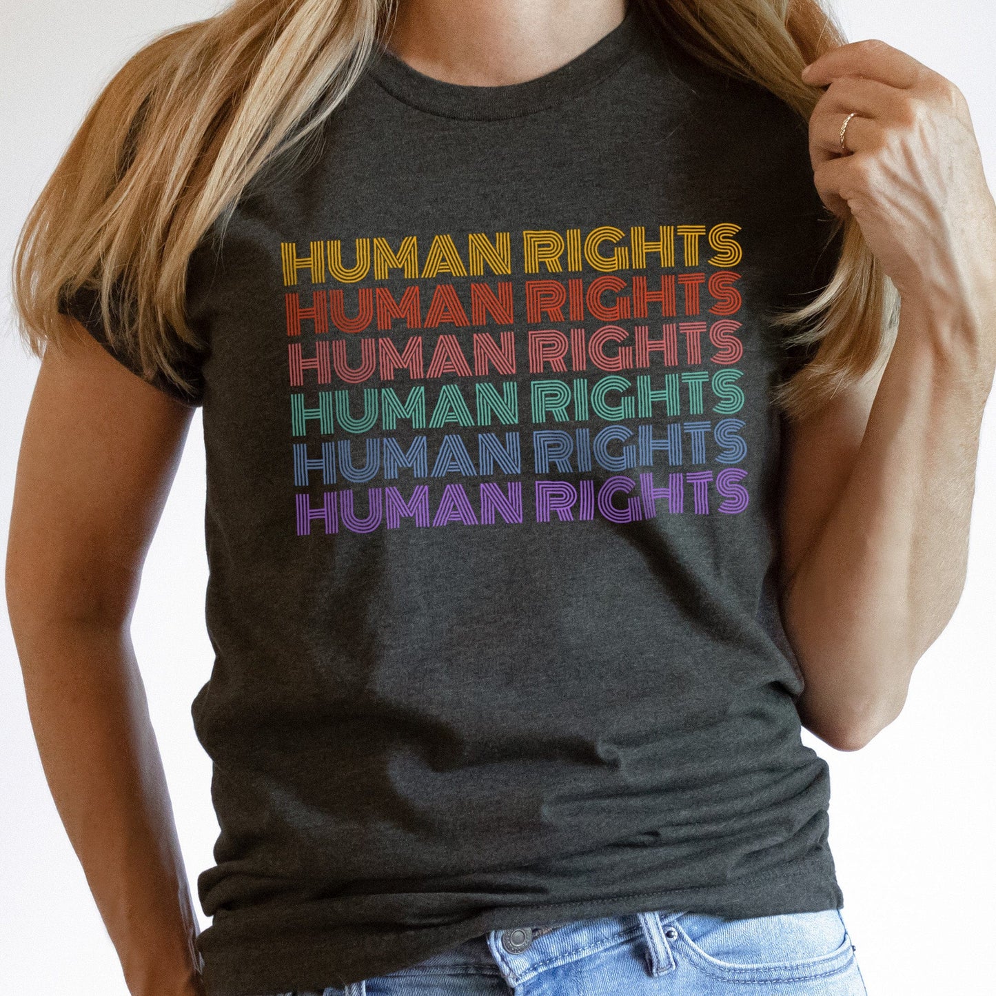 Dark Grey Heather color unisex t-shirt that says, “HUMAN RIGHTS” six times. The first row is yellow, the second row is burgundy/red, the third row is dark pink, the fourth row is teal, the fifth row is dark blue, and the last row is purple.