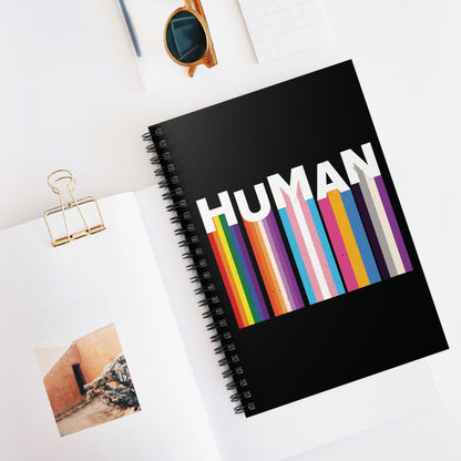 Contextual photo of a 118-page spiral bound notebook with a black cover. It has a colorful and dynamic image featuring the word "HUMAN" written in an artistic style.  Each letter is arranged to create a wavy pattern. There are stripes of colors coming down from the bottom of each letter representing different sexualities in the LGBTQ+ community. The "H" represents Gay, the "U" represents Lesbian, the "M" represents Trans, the "A" represents Pansexual, and the "N" represents Asexual.