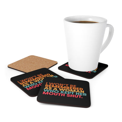 Four 3.75” x 3.75” black square coasters that say, “I won’t be remembered as a woman who kept her mouth shut” in all caps. The phrase is on 5 lines, with each line being a different color. “I won’t be” is brown, “remembered” is orange, “as a woman” is yellow-orange, “who kept her” is blue-green, and “mouth shut” is pink-red.  There’s a white mug on one of them.