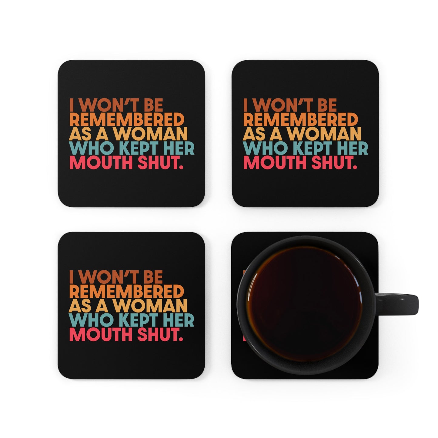 Four 3.75” x 3.75” black square coasters that say, ““I won’t be remembered as a woman who kept her mouth shut” in all caps. The phrase is on 5 lines, with each line being a different color. “I won’t be” is brown, “remembered” is orange, “as a woman” is yellow-orange, “who kept her” is blue-green, and “mouth shut” is pink-red. The image is from an overhead perspective, and the coasters are arranged in a group with one that has a black coffee mug on it.