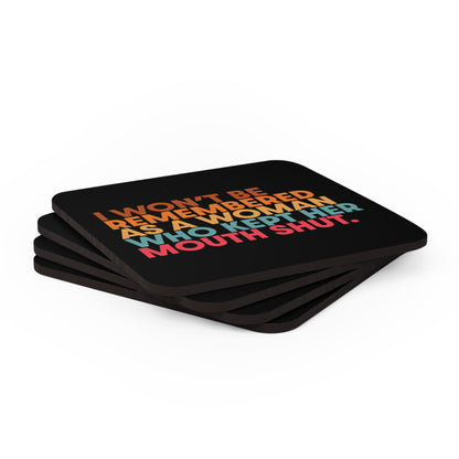 Four 3.75” x 3.75” black square coasters that say, “I won’t be remembered as a woman who kept her mouth shut” in all caps. The phrase is on 5 lines, with each line being a different color. “I won’t be” is brown, “remembered” is orange, “as a woman” is yellow-orange, “who kept her” is blue-green, and “mouth shut” is pink-red. The coasters are shown at an angle.