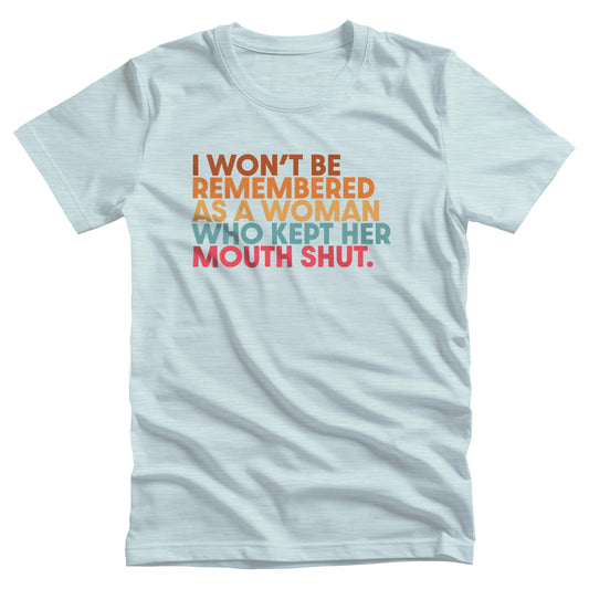 Heather Ice Blue color unisex t-shirt that says, “I won’t be remembered as a woman who kept her mouth shut” in all caps. The phrase is on 5 lines, with each line being a different color. “I won’t be” is brown, “remembered” is orange, “as a woman” is yellow-orange, “who kept her” is blue-green, and “mouth shut” is pink-red. 
