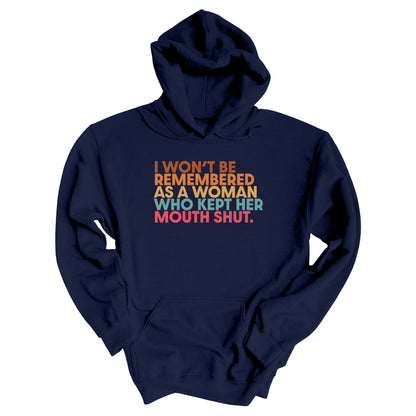 Navy Blue hoodie that says, “I won’t be remembered as a woman who kept her mouth shut” in all caps. The phrase is on 5 lines, with each line being a different color. “I won’t be” is brown, “remembered” is orange, “as a woman” is yellow-orange, “who kept her” is blue-green, and “mouth shut” is pink-red. 