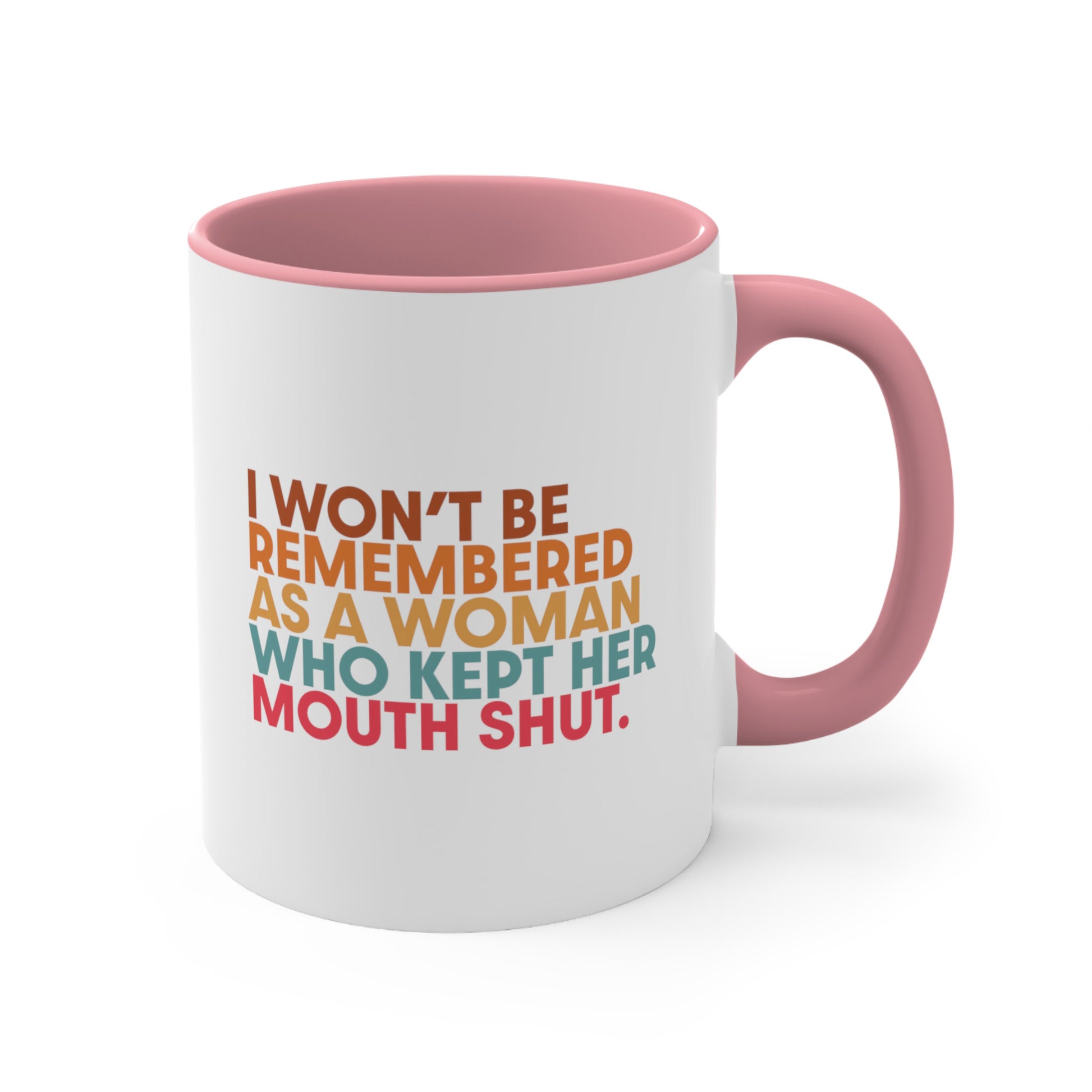 11oz ceramic mug with a pink handle and interior that says, “I won’t be remembered as a woman who kept her mouth shut” in all caps. The phrase is on 5 lines, with each line being a different color. “I won’t be” is brown, “remembered” is orange, “as a woman” is yellow-orange, “who kept her” is blue-green, and “mouth shut” is pink-red. 