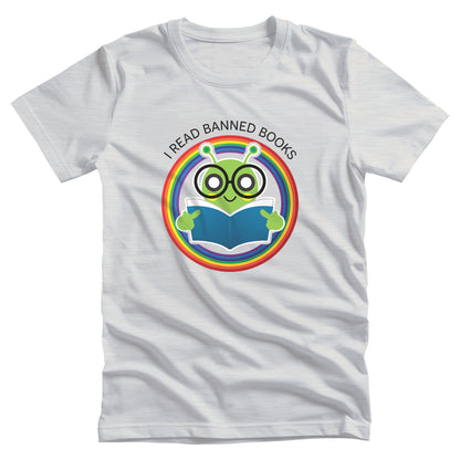 Ash color unisex t-shirt with a graphic of a bookworm with large eyeglasses reading a book. The bookworm is subtly holding up its middle fingers. The image is inside a circle that has rainbow colors. Arched over the top of the graphic are the words “I READ BANNED BOOKS.”