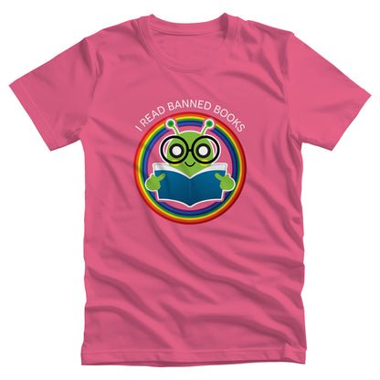 Charity Pink color unisex t-shirt with a graphic of a bookworm with large eyeglasses reading a book. The bookworm is subtly holding up its middle fingers. The image is inside a circle that has rainbow colors. Arched over the top of the graphic are the words “I READ BANNED BOOKS.”