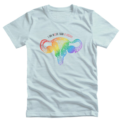 Heather Ice Blue color unisex t-shirt that says, “I am More Than a Uterus” in all caps. The “O” in “more” is the symbol for the female gender. The text is arched slightly over an illustration of a uterus made from swirls and flowers in a rainbow-gradient color.