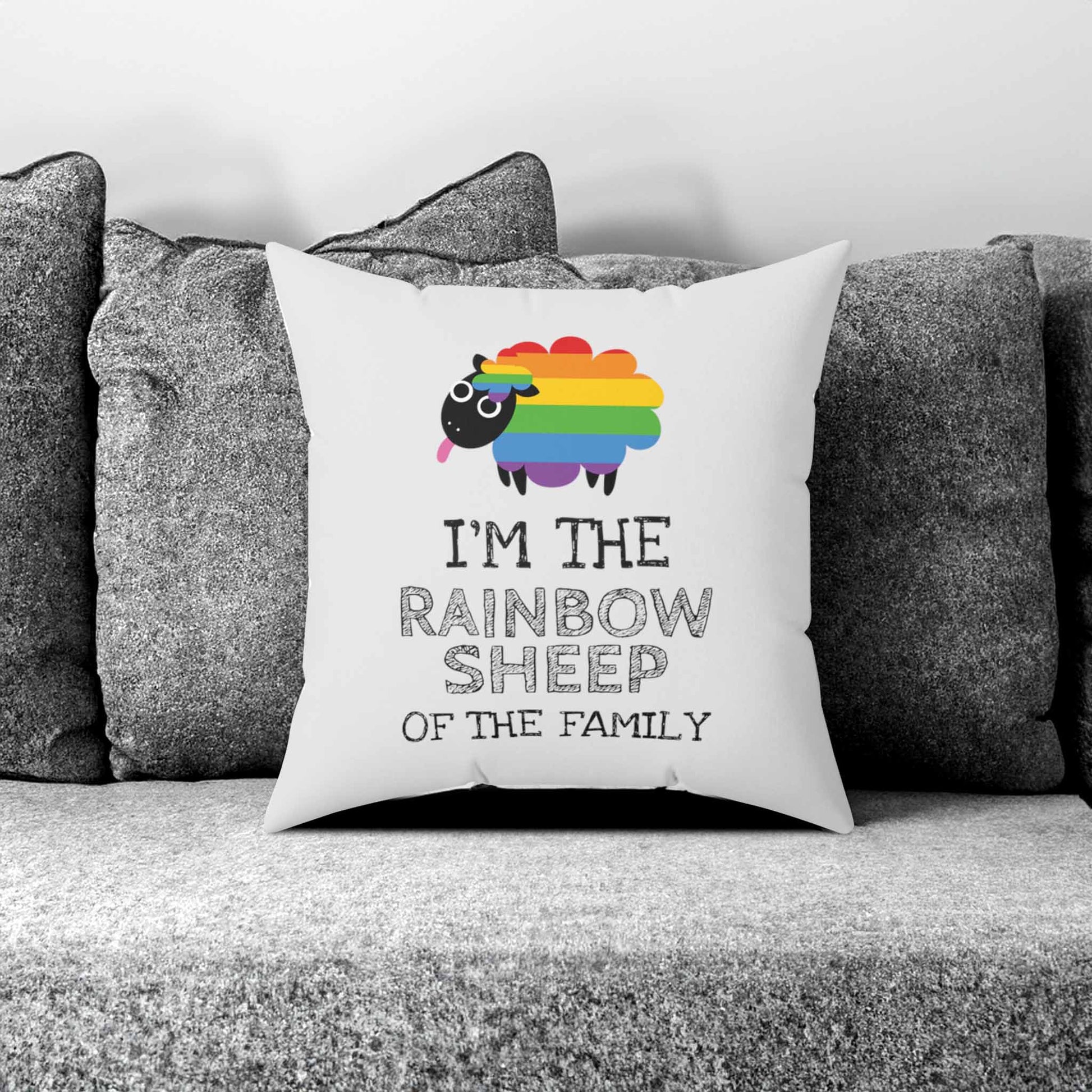Contextual photo of a very light grey 14x14 inch square pillow. Not shown in the photo is the front of the pillow, which says, “I’m the rainbow sheep of the family” with a graphic of a rainbow-colored sheep above it. The pillow is on a gray couch.