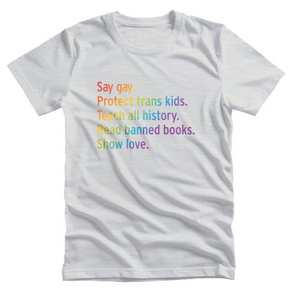 Ash color unisex tank top with text that says “Say gay. Protect Trans Kids. Teach all history. Read banned books. Show love.” Each sentence is on its own line, and the entire graphic is colored with a rainbow gradient.