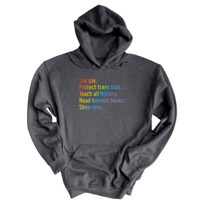 Dark Heather color unisex hoodie with text that says “Say gay. Protect Trans Kids. Teach all history. Read banned books. Show love.” Each sentence is on its own line, and the entire graphic is colored with a rainbow gradient.