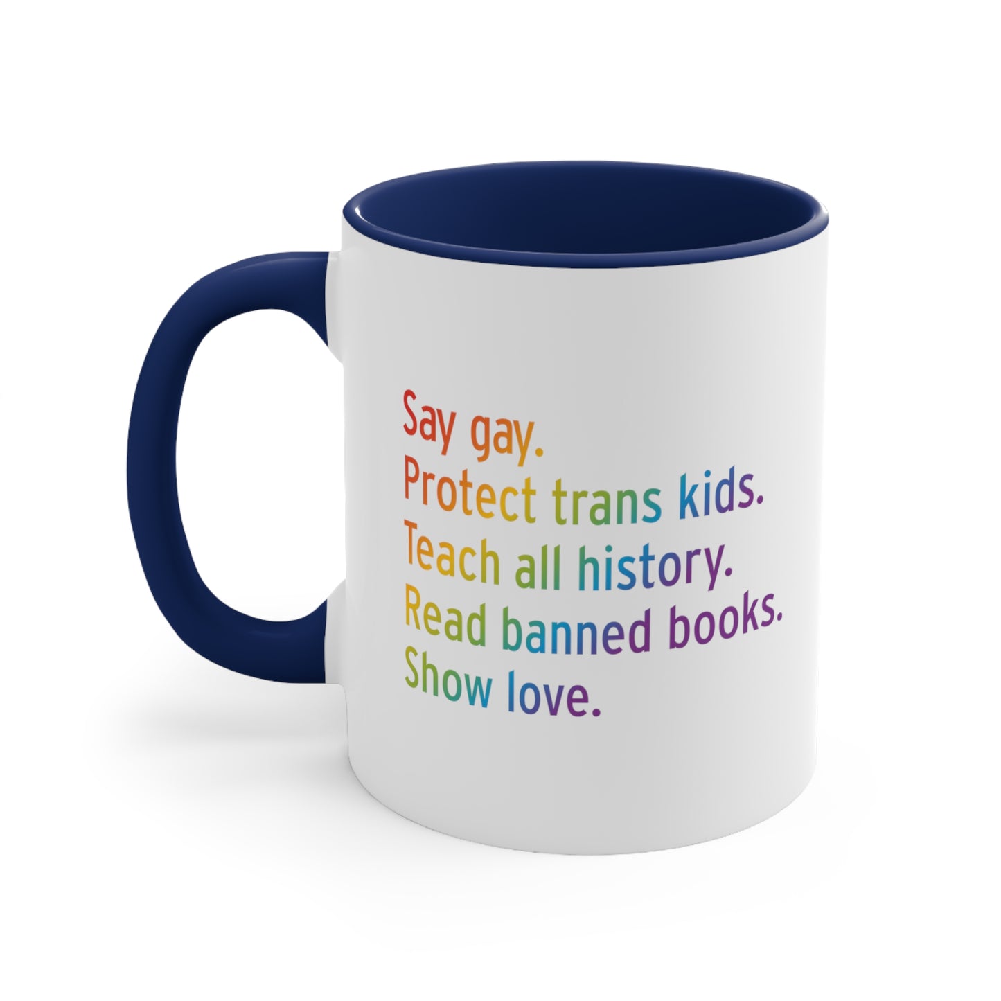 11oz white ceramic mug colored navy blue on the inside of the mug and the handle. The text says “Say gay. Protect Trans Kids. Teach all history. Read banned books. Show love.” Each sentence is on its own line, and the entire graphic is colored with a rainbow gradient.