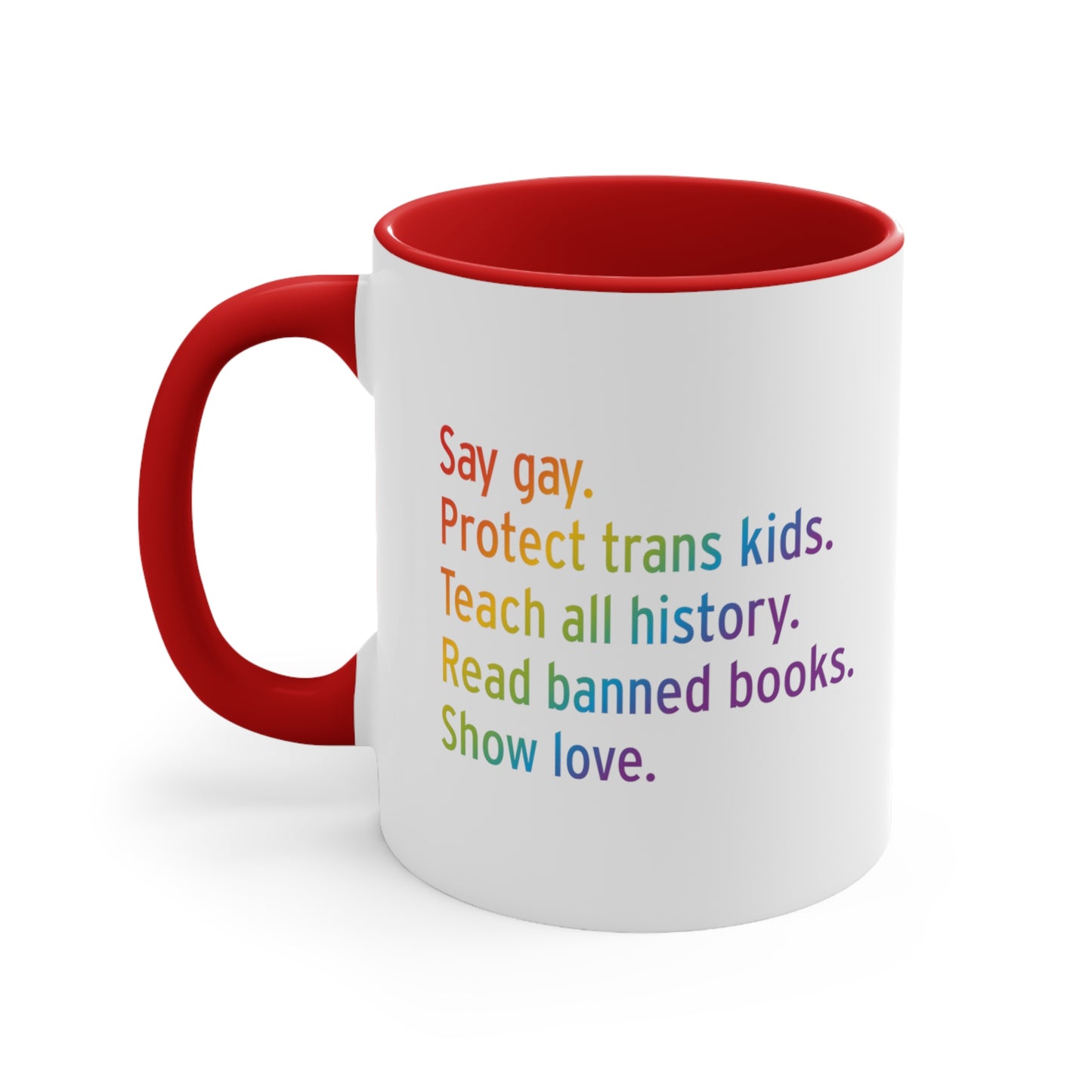 11oz white ceramic mug colored red on the inside of the mug and the handle. The text says “Say gay. Protect Trans Kids. Teach all history. Read banned books. Show love.” Each sentence is on its own line, and the entire graphic is colored with a rainbow gradient.