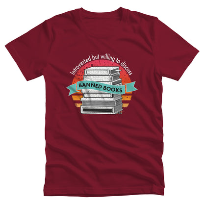 Cardinal color unisex t-shirt with a graphic that says, “Introverted but willing to discuss banned books.” The image has stacked books with a circular retro sunset behind it. “Introverted but willing to discuss” is arched over the graphic, and “banned books” is inside a wavey blue-green colored ribbon.