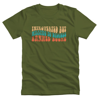 Olive color unisex t-shirt with a graphic that says “Introverted but willing to discuss banned books” in a retro, 1970s bubble font. Each line is a different color. The graphic is slightly distressed.