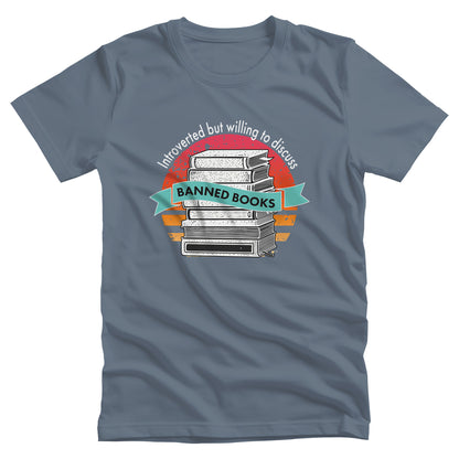 Steel Blue color unisex t-shirt with a graphic that says, “Introverted but willing to discuss banned books.” The image has stacked books with a circular retro sunset behind it. “Introverted but willing to discuss” is arched over the graphic, and “banned books” is inside a wavey blue-green colored ribbon.