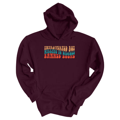 Maroon unisex hoodie with a graphic that says “Introverted but willing to discuss banned books” in a retro, 1970s bubble font. Each line is a different color. The graphic is slightly distressed.