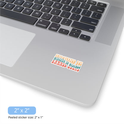 Contextual photo of the 2x2 inch (2x1” peeled) kiss-cut sticker that says “Introverted but willing to discuss banned books” in a retro, 1970s bubble font. Each line is a different color. The graphic is slightly distressed.