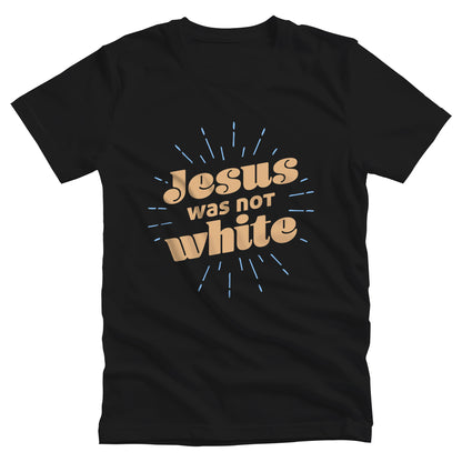 Black unisex t-shirt that says, “Jesus was not white” in over a blue-green starburst. The text is thick, has curls, and is slanted upwards.