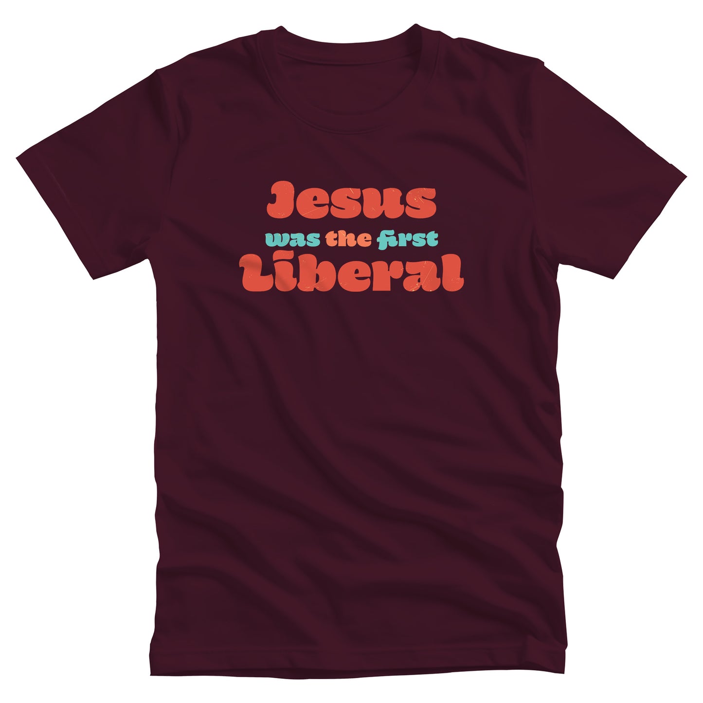 Maroon unisex t-shirt that says, “Jesus was the first Liberal.” The words “Jesus”, “the”, and “Liberal” are all a shade of orange, and the words “Was” and “First” are a light blue-green.