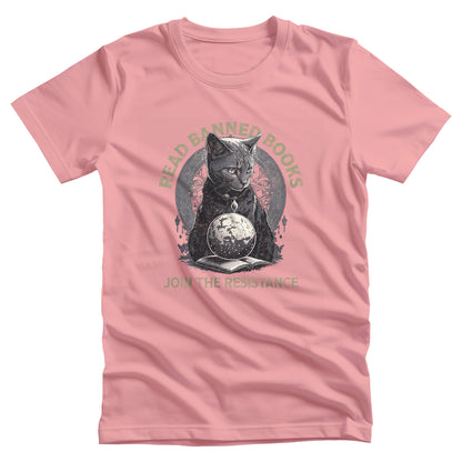 Pink unisex t-shirt with a graphic of a cat sitting over a globe and an open book. The text says “Read banned books” arched over the top of the cat and “Join the resistance” in a line under the graphic. The text is in all caps.