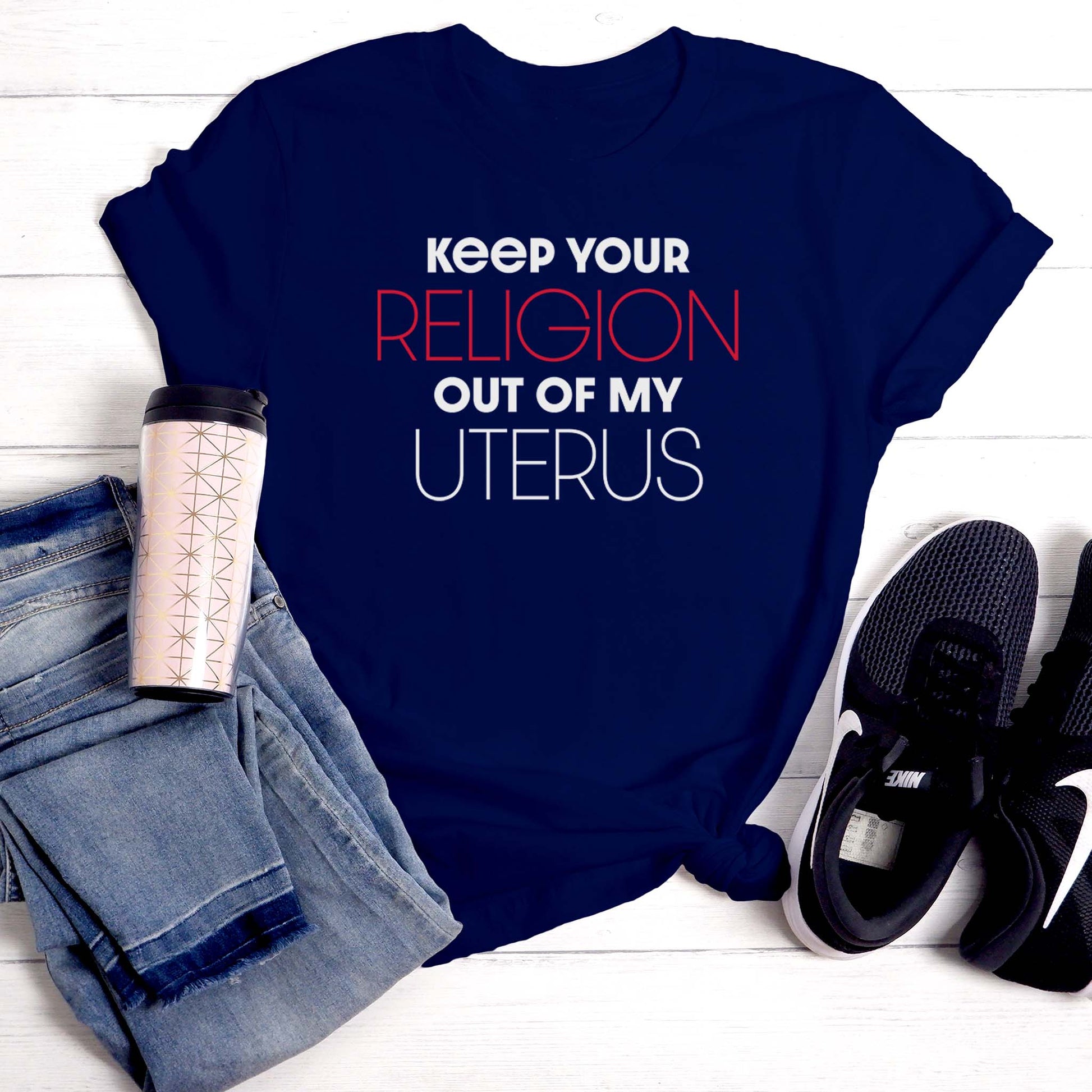 Navy unisex t-shirt that says, “Keep Your Religion Out of My Uterus” in all caps. “Keep Your” is bold, “Religion” is on the next line, is a larger size, and is red, “out of my” is beneath that and in bold, and “uterus” is on the last line