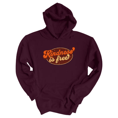 Maroon unisex hoodie with a retro graphic that says “Kindness is free.” The text is in a script font with a brown oval behind it. The “k” and the “s” in the word “Kindness” are not contained inside the oval. The graphic is also distressed to add to the retro feel.
