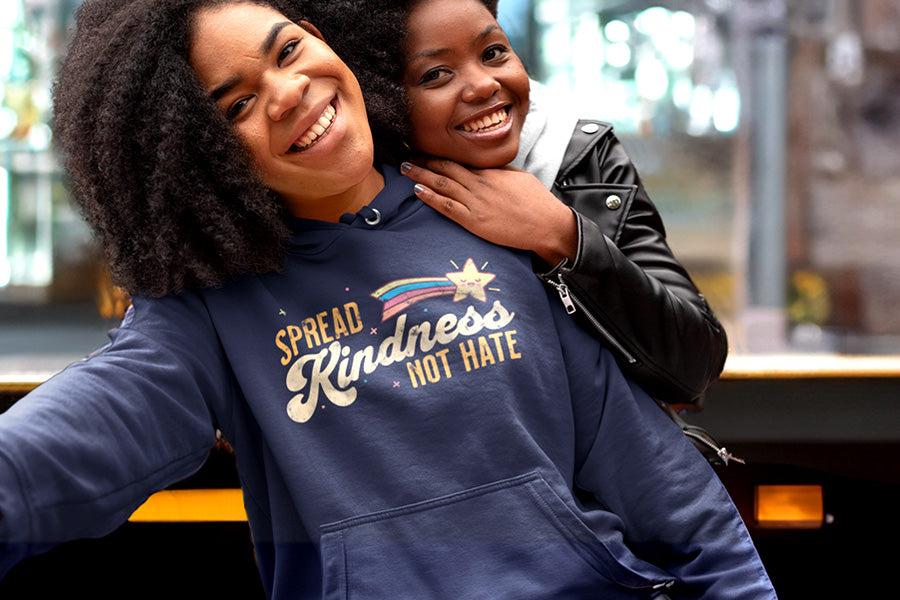 Two friends hanging out with one wearing a kindness hoodie. The graphic on the front says, "Spread kindness not hate" with a shooting star beside "SPREAD" and above "kindness." The word "kindness" is in a script font, the rest is all caps.
