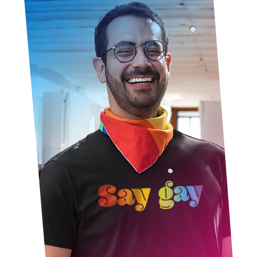 A a man wearing a unisex t-shirt that says, "Say gay" in a rainbow colored gradient. He also has on a rainbow scarf.