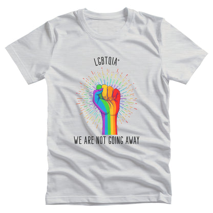 Ash color unisex t-shirt that says, “LGBTQIA+ We Are Not Going Away” with a graphic of a rainbow fist with a rainbow-gradient color starburst behind it. Slightly arched over the starburst are the words “LGBTQIA+” and the rest of the text is below the graphic in one horizontal line.