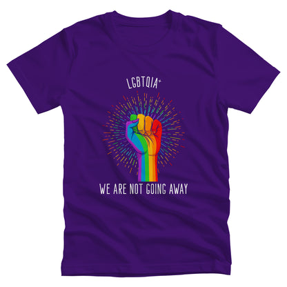 Team Purple color unisex t-shirt that says, “LGBTQIA+ We Are Not Going Away” with a graphic of a rainbow fist with a rainbow-gradient color starburst behind it. Slightly arched over the starburst are the words “LGBTQIA+” and the rest of the text is below the graphic in one horizontal line.