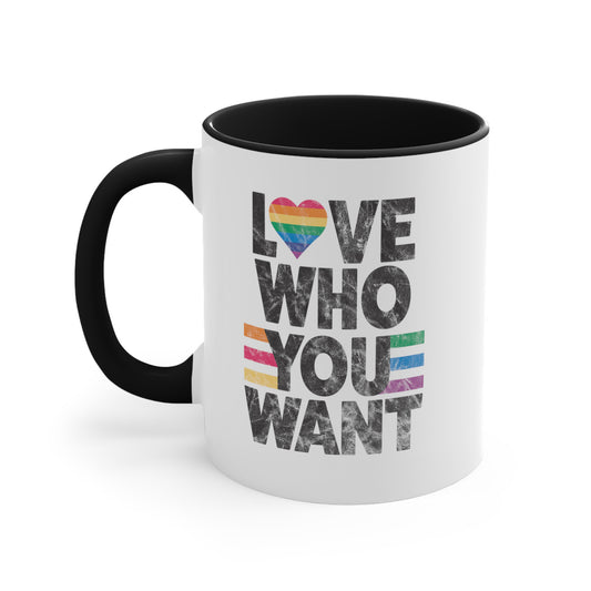 11oz ceramic mug with a black interior and handle says, “Love who you want” in all caps. Each word is on its own line. The “O” in “love” is a rainbow heart.