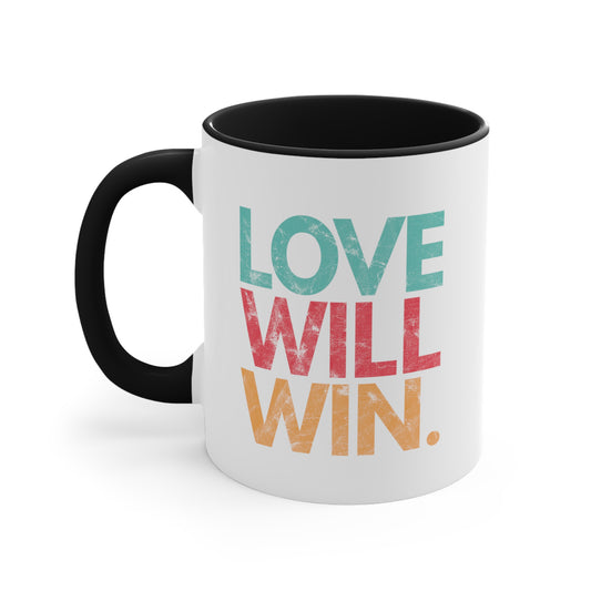 11oz ceramic mug with a black handle and interior with a graphic that says “Love will win.” in all caps. Each word is on its own line and is a different color. “Love” is greenish-blue, “Will” is red, and “Win.” is yellow. The graphic has a faded and slightly grungy/worn look.