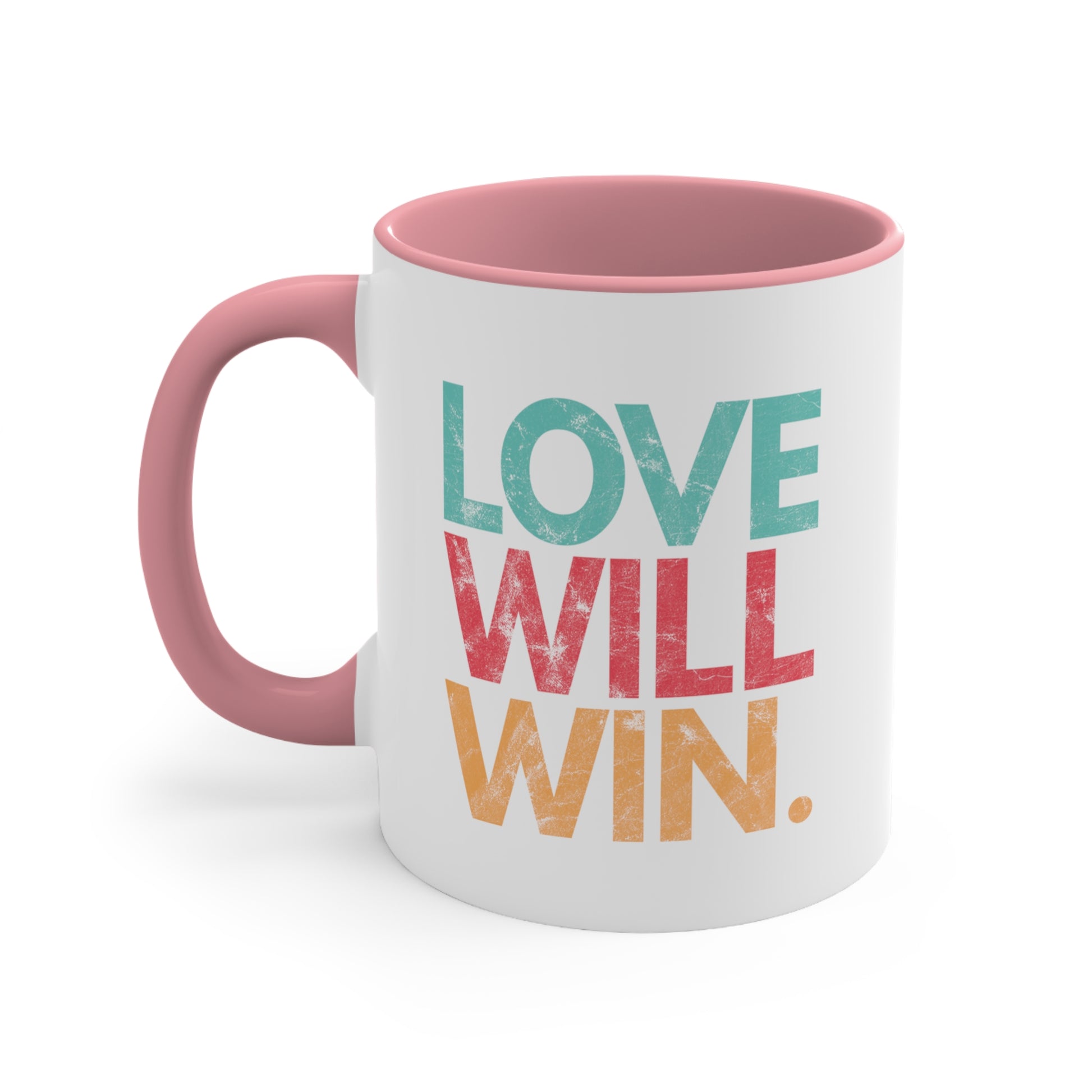 11oz ceramic mug with a pink handle and interior with a graphic that says “Love will win.” in all caps. Each word is on its own line and is a different color. “Love” is greenish-blue, “Will” is red, and “Win.” is yellow. The graphic has a faded and slightly grungy/worn look.