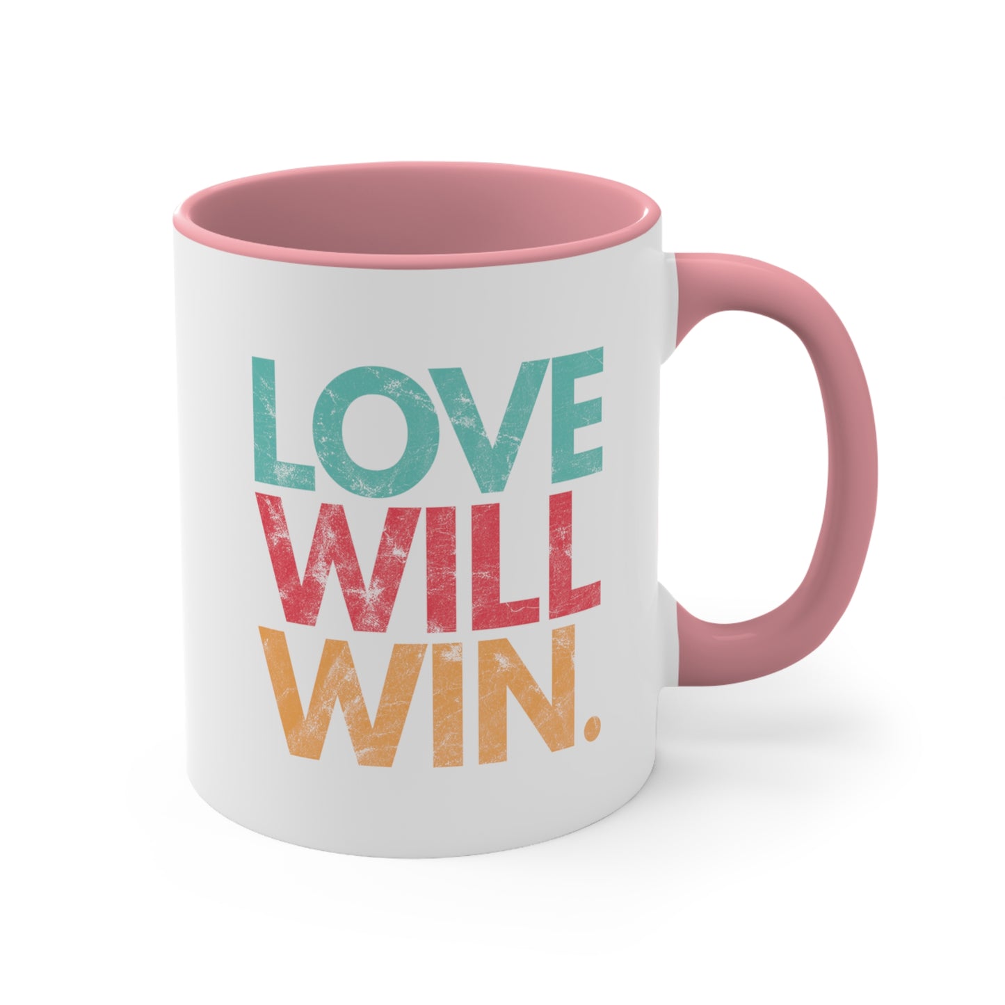 11oz ceramic mug with a pink handle and interior with a graphic that says “Love will win.” in all caps. Each word is on its own line and is a different color. “Love” is greenish-blue, “Will” is red, and “Win.” is yellow. The graphic has a faded and slightly grungy/worn look.