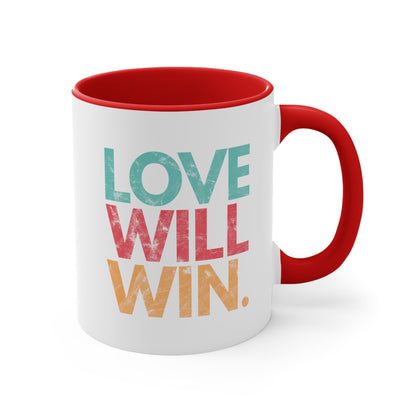 11oz ceramic mug with a red handle and interior with a graphic that says “Love will win.” in all caps. Each word is on its own line and is a different color. “Love” is greenish-blue, “Will” is red, and “Win.” is yellow. The graphic has a faded and slightly grungy/worn look.