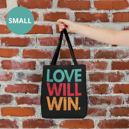 Black tote bag with a graphic that says “Love will win.” in all caps. Each word is on its own line and is a different color. “Love” is greenish-blue, “Will” is red, and “Win.” is yellow. The graphic has a faded and slightly grungy/worn look.