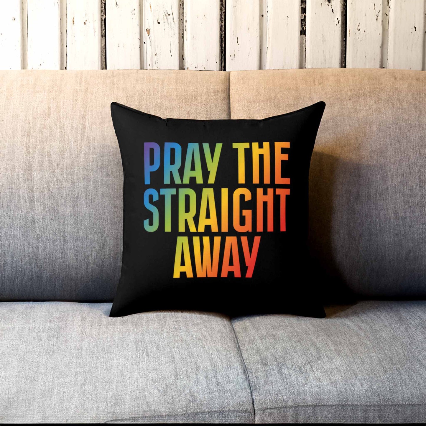 Contextual photo of a 14x14” black square decorative pillow that says, “PRAY THE STRAIGHT AWAY” in a bold font with gradient rainbow colors. The pillow is on a couch.