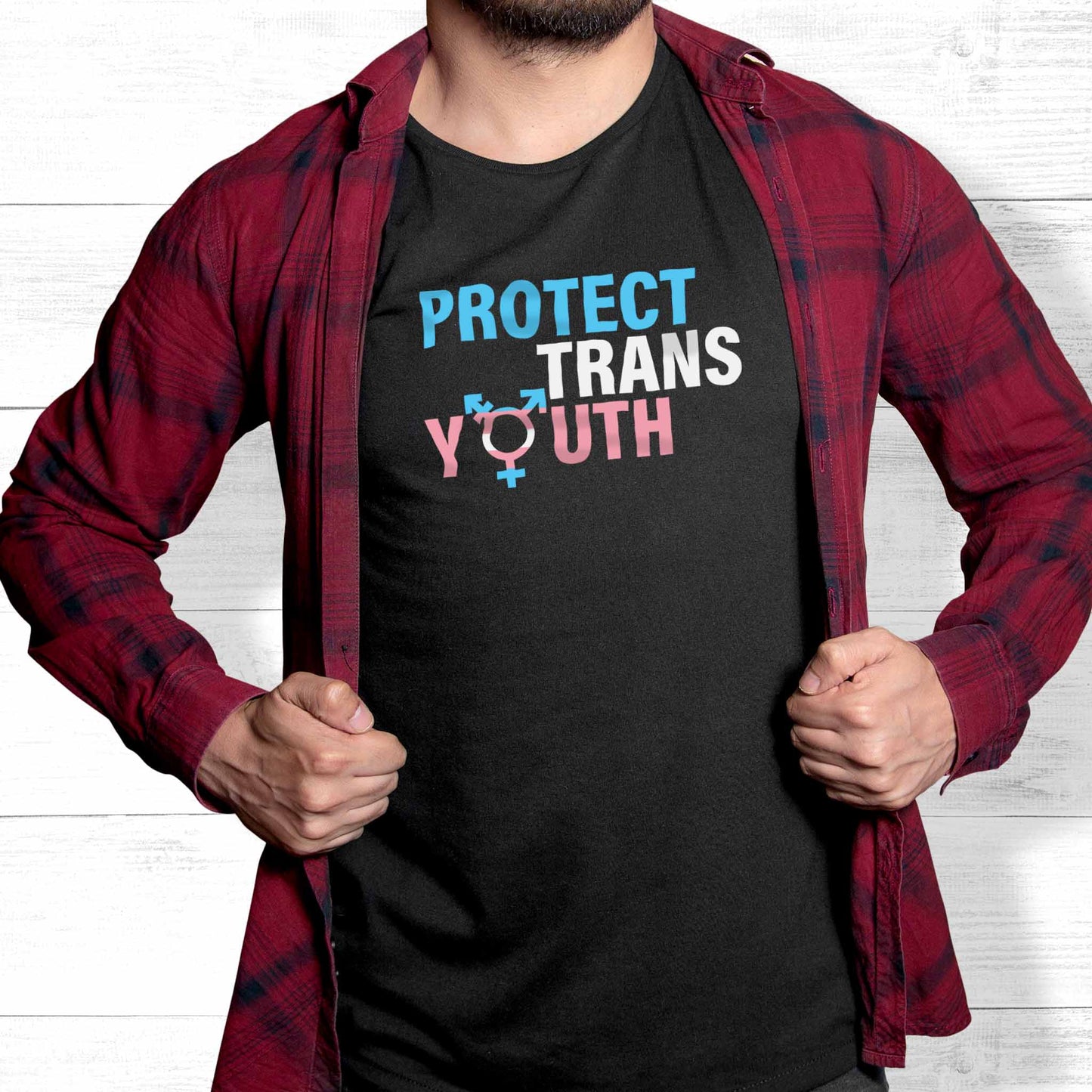 Black unisex t-shirt that says, “Protect Trans Youth” in all caps. Each word is on its own line. Each line correlates to the trans flag colors. The  “O” in the word “Youth” is the trans symbol.