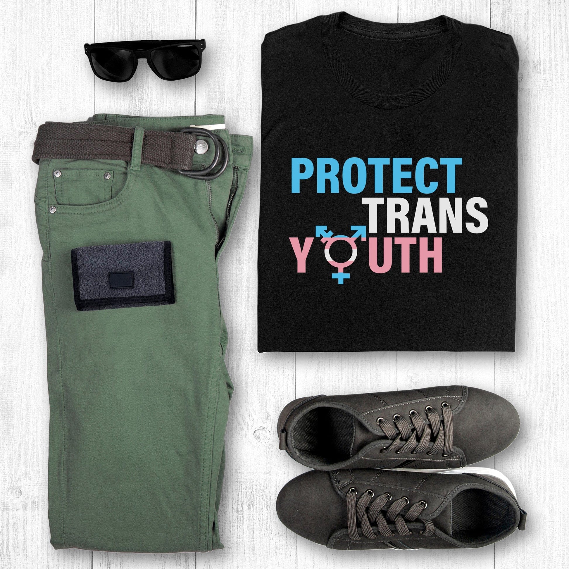 Black unisex t-shirt that says, “Protect Trans Youth” in all caps. Each word is on its own line. Each line correlates to the trans flag colors. The  “O” in the word “Youth” is the trans symbol.