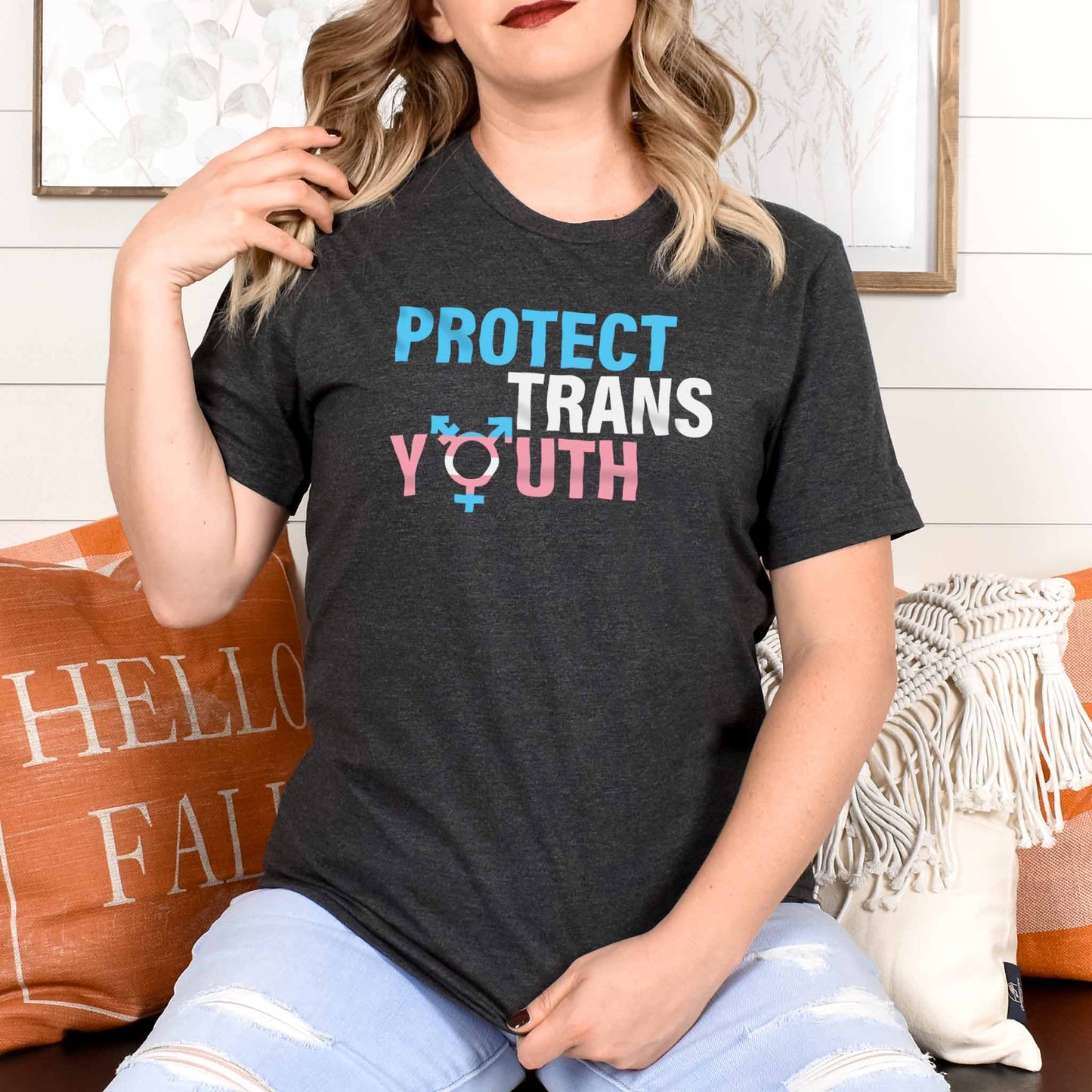 Dark Grey Heather color unisex t-shirt that says, “Protect Trans Youth” in all caps. Each word is on its own line. Each line correlates to the trans flag colors. The  “O” in the word “Youth” is the trans symbol.