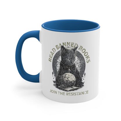 11oz ceramic mug with a blue interior and handle with a graphic of a cat sitting over a globe and an open book. The text says “Read banned books” arched over the top of the cat and “Join the resistance” in a line under the graphic. The text is in all caps.