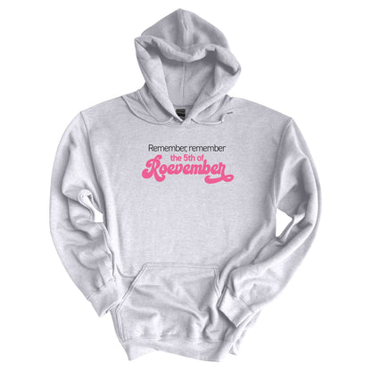 Ash color hoodie featuring the phrase 'Remember, Remember the 5th of Roevember'. The text 'The 5th of Roevember' is highlighted in pink, embellished with a decorative script font and additional swooshes.\