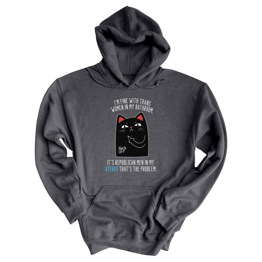 Dark Grey Heather color unisex hoodie with a graphic of an annoyed cat showing its middle finger. The text says “I’m fine with trans women in my bathroom” above the graphic, slightly arched. Below the graphic reads “It’s Republican men in my uterus that’s the problem.”