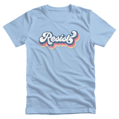 Baby Blue color unisex t-shirt that says, “Resist” in a script font and thickly outlined with four colors which have been shifted downward to give it a retro feel.  The colors are dark blue, dark pink, and beige. (There is also a light blue outline but it isn’t noticeable since it’s the same color as the shirt.)