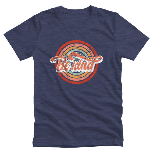 Heather Navy color unisex t-shirt with a graphic that says “Be Kind.” There is a retro-colored circular rainbow behind it. The text is outlined in white and has a long swoosh that swirls from the end of the letter “d” across the entire word “kind.”