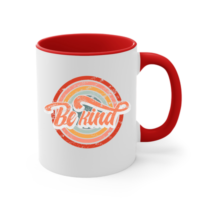 11oz white ceramic mug with a red handle and interior that says “Be Kind.” There is a retro-colored circular rainbow behind it. The text is outlined in white and has a long swoosh that swirls from the end of the letter “d” across the entire word “kind.”