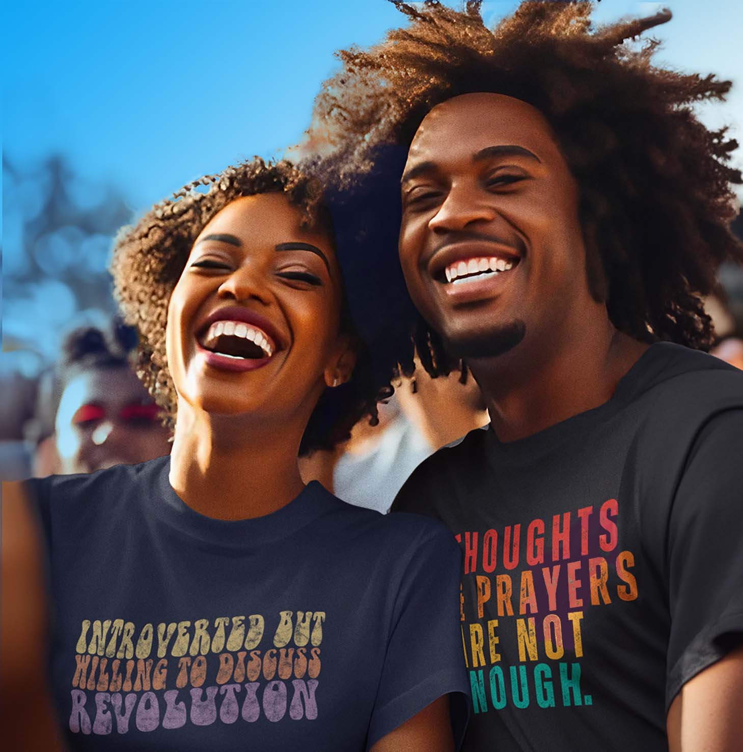 A Black man in a woman wearing unisex T-shirts. The woman's shirt says, "INTROVERTED BUT WILLING TO DISCUSS REVOLUTION.” the man's shirt says, “THOUGHTS AND PRAYERS ARE NOT ENOUGH.”
